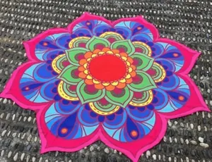 Vue détaillée d'une serviette de plage mandala colorée sur un sol de galets gris.
