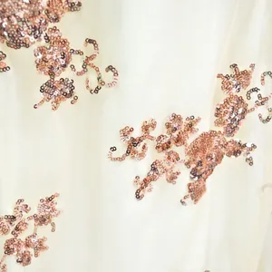 Close-up of intricate rose gold sequins on elegant cream mesh fabric for a luxury evening gown