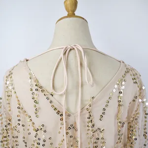 Detailed back view of a beige mesh dress featuring shimmering gold sequin tassels