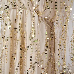 Detailed macro shot showcasing shimmering gold sequins and tassels on a beige mesh long dress