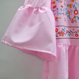 Gros plan du motif floral vibrant sur une robe bohème rose aux manches cloches évasées