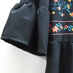 Détail en gros plan montrant l'imprimé floral ethnique et la manche cloche de la robe noire trapèze
