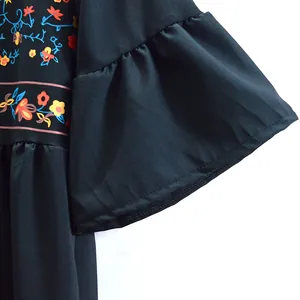 Détail d'une robe noire de style ethnique avec imprimés floraux et manches cloches.