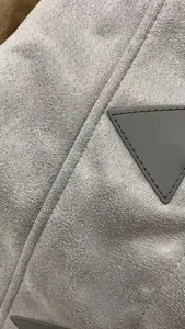 Close-up of gray suede texture and triangular patch detail on women's hooded winter coat.