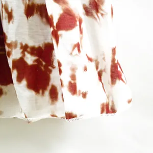 Detailed macro view of the brown tie-dye print and stitched hem on a white vacation dress
