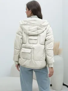 Back view of a women's beige hooded puffer jacket with unique quilted pocket details.