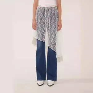Dettaglio di una gonna asimmetrica in pizzo bianco sovrapposta a jeans in denim blu