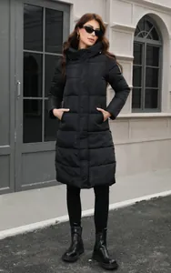 Full-length view of a women's black hooded puffer coat in a street style setting.