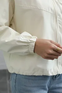 Close-up detail of a cream waterproof windbreaker jacket with elastic cuffs and zipper