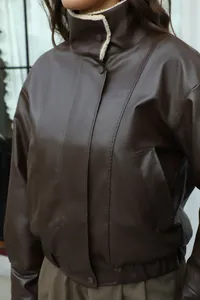 Primer plano de chaqueta de cuero sintético marrón con detalle de cuello de borrego crema.