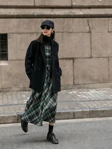 Style de rue d'une femme portant un blazer en velours côtelé noir et une robe à carreaux.