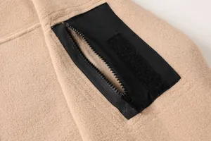 Primo piano della tasca con cerniera e velcro su felpa tattica in pile kaki.