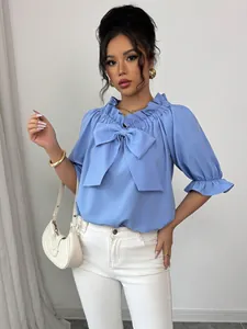 Blouse élégante bleu clair à col volanté avec un grand nœud et manches bouffantes.