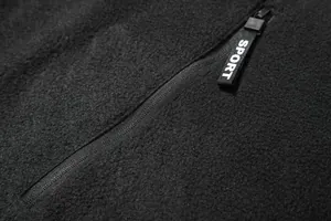 Makro-Detailansicht eines Reißverschlusses mit SPORT-Tag an einem schwarzen Fleecepullover