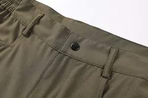 Macro detail of men's olive cargo pants showing ripstop fabric and button closure