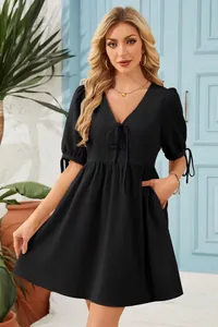 Elegant black V-neck tie-front mini dress with short puff sleeves shown on model outdoors
