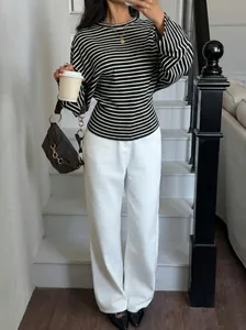 Woman posing on stairs in a striped batwing sleeve top and white trousers outfit
