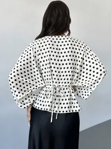 Back view of elegant white polka dot blouse with batwing sleeves and waist tie detail.