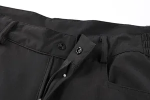 Close-up of black functional cargo pants showing zipper and durable snap button closure.