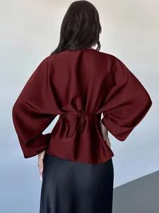 Detail back view of burgundy satin long-sleeve blouse with tie-back waist design.