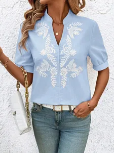 Close-up detail of delicate white floral embroidery on light blue V-neck cotton shirt