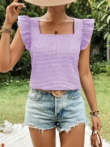Detailed view of purple gingham blouse with square neck and ruffle sleeves in a garden