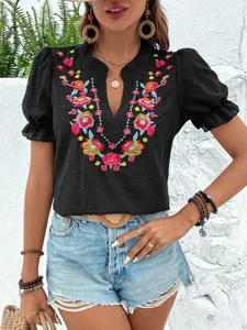 Primer plano del bordado floral en una blusa negra con cuello en V y mangas abullonadas.
