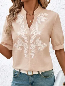 Detail of women's beige cotton shirt with white floral embroidery and V-neckline.
