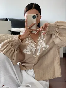 Nahaufnahme einer beige bestickten Langarmbluse mit eleganter, geblümter Knopfleiste