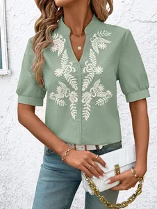 Close-up of mint green V-neck blouse featuring intricate white floral embroidery on cotton.