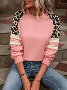 Détail d'un sweat-shirt rose avec manches raglan léopard et poignets rayés sur escalier.