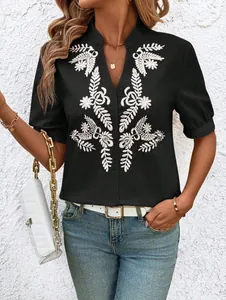 Detailed view of women's black V-neck cotton blouse with white floral embroidery.