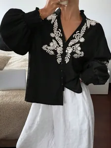 Detailaufnahme der schwarzen Bluse mit weißer Stickerei und feinen Knopfleisten