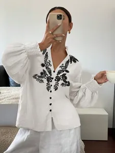 Detailaufnahme der weißen Bluse mit schwarzen Stickereien und eleganten Knopfleisten