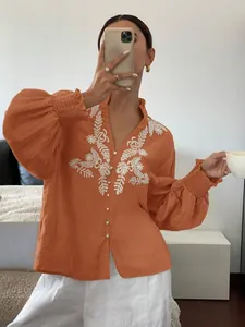 Detail eines orangefarbenen Langarmshirts mit weißer Blumenstickerei und Knopfleiste