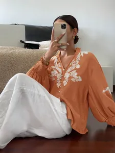 Detail der schicken orangefarbenen Bluse mit weißer Blumenstickerei und Knopfleiste vorne.