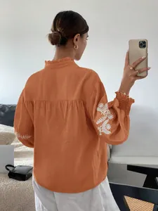 Detaillierte Rückansicht einer orangefarbenen Herbstbluse mit eleganter weißer Ärmelstickerei.