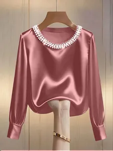 Close-up detail of an elegant mauve pink satin blouse featuring a pearl-embellished round neckline.