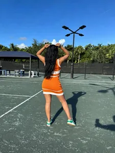 Vista trasera de mujer en minivestido de punto naranja y blanco sin mangas en cancha de tenis