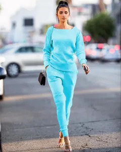 Full-body view of a model wearing a bright cyan knit two-piece set on a sunny city street