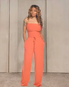 Chic combinaison bustier orange vif à jambes larges portée par un mannequin sur mur gris