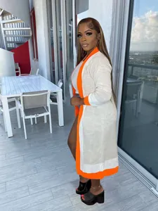 Elegant long knit cardigan with vibrant orange trim worn by a model on a balcony.