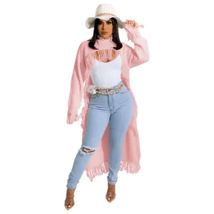 Full-length view of a women's long pink fringe cardigan styled with denim jeans.