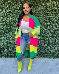 Gilet en maille color-block oversize aux couleurs vives sur fond de feuillage vert.