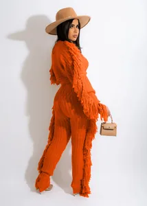 Detailed view of bright orange cable knit set featuring fringe details on sleeves and pants
