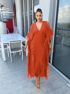 Detail view of a model wearing an orange handmade crochet tassel maxi dress on a balcony