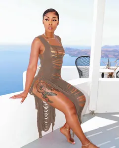 Modell trägt ein braunes, gestricktes Strandkleid mit Fransen und Cut-outs auf Balkon