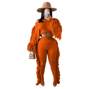 Close-up detail of a bright orange two-piece knitted set featuring stylish long fringe tassels