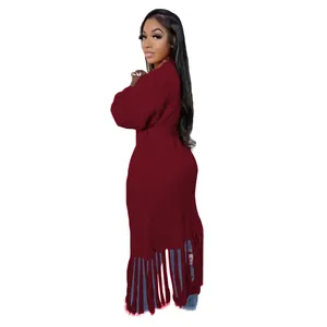 Detail view of a long maroon knit cardigan sweater featuring a decorative fringe hem.