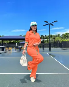 Ensemble en maille orange vif comprenant un polo et un pantalon large sur un court de tennis.